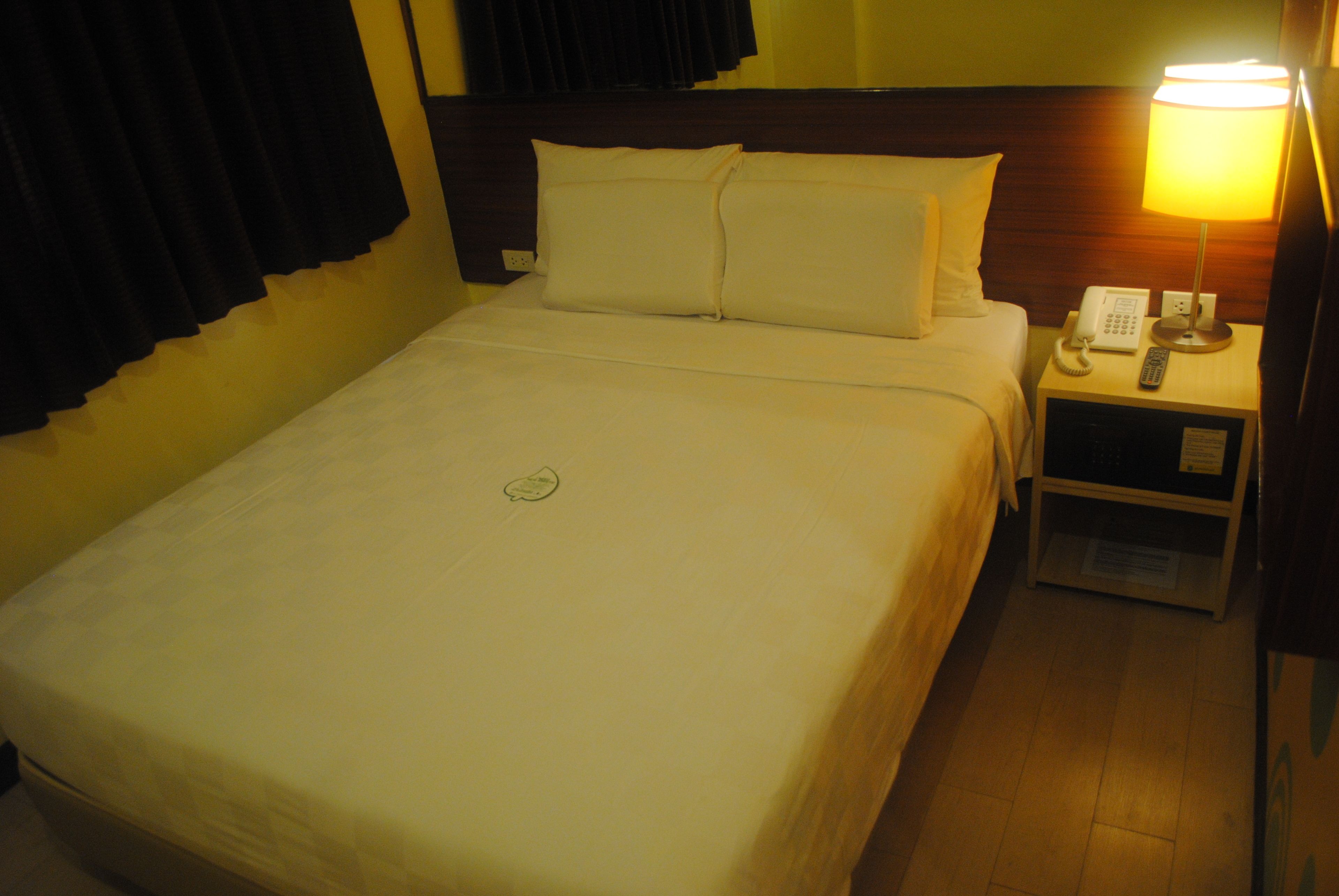 A hotel room with a neatly made bed, a bedside table with a lamp, and a phone.