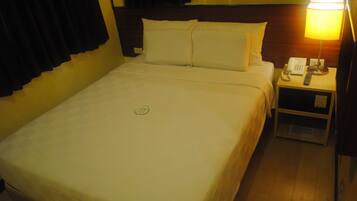 A hotel room with a neatly made bed, a bedside table with a lamp, and a phone.