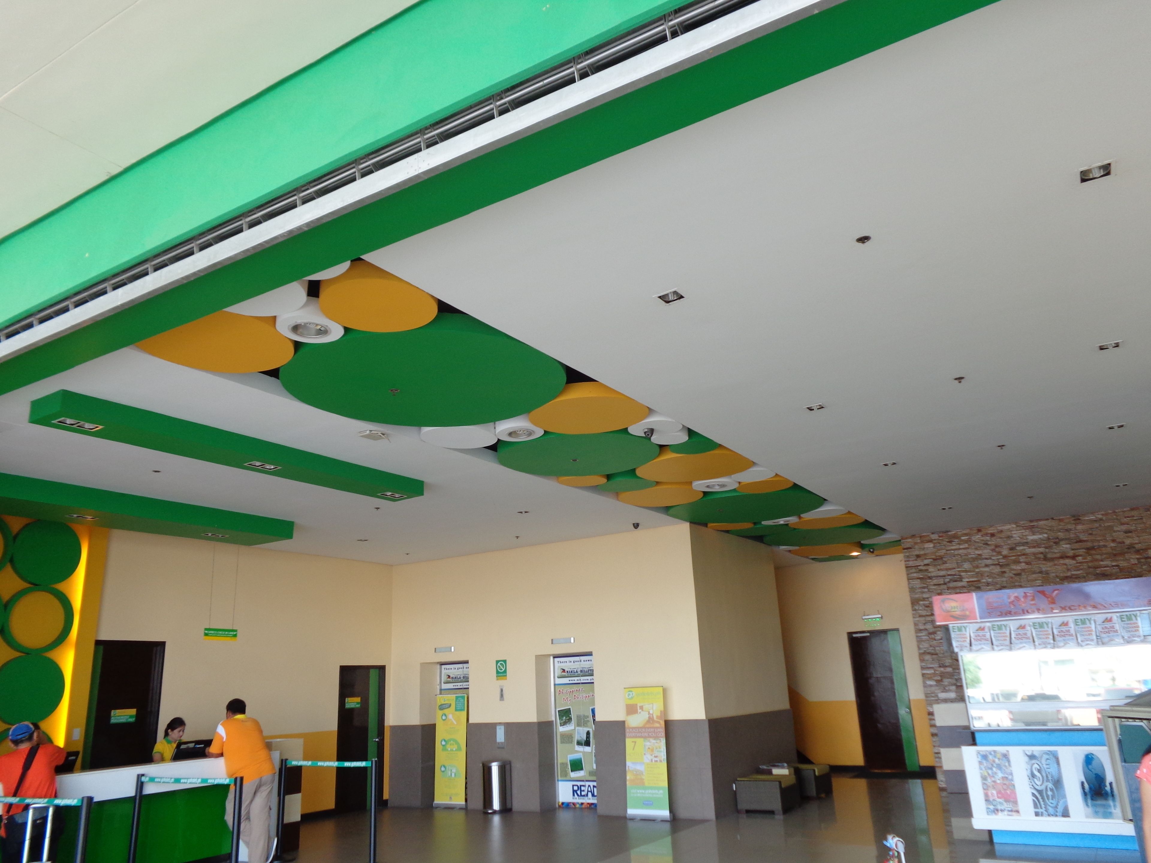 Un área de recepción con una decoración en tonos verde y blanco, una recepción con personal y una pared con un cartel.