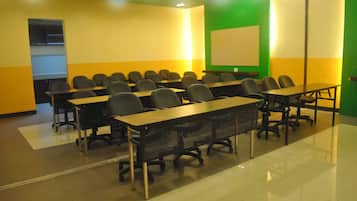 A conference room with rows of tables and chairs, a whiteboard, and a green accent wall.