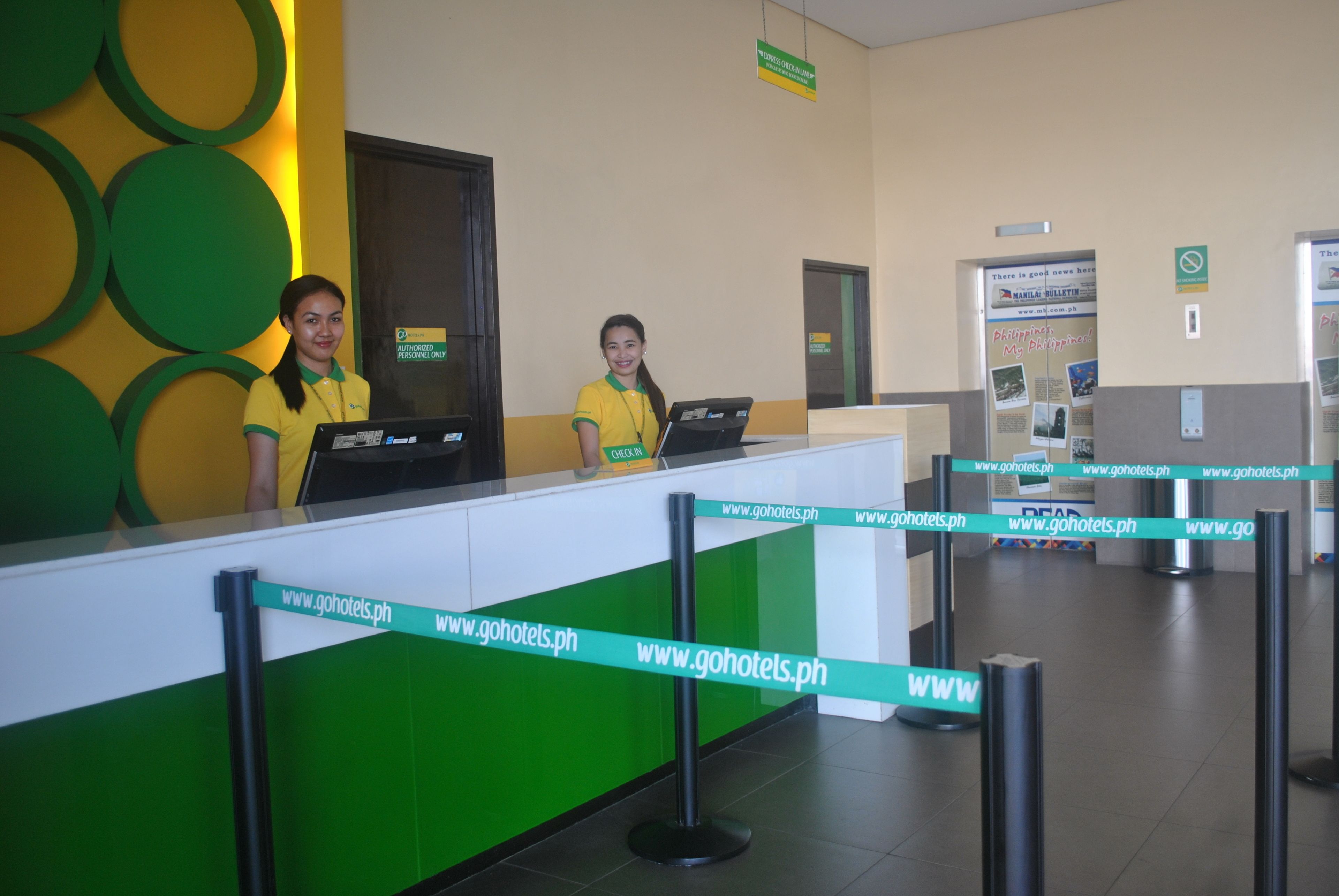 A reception desk with a green and white color scheme, two receptionists in yellow uniforms, and a sign indicating 'Authorized Personnel Only'.