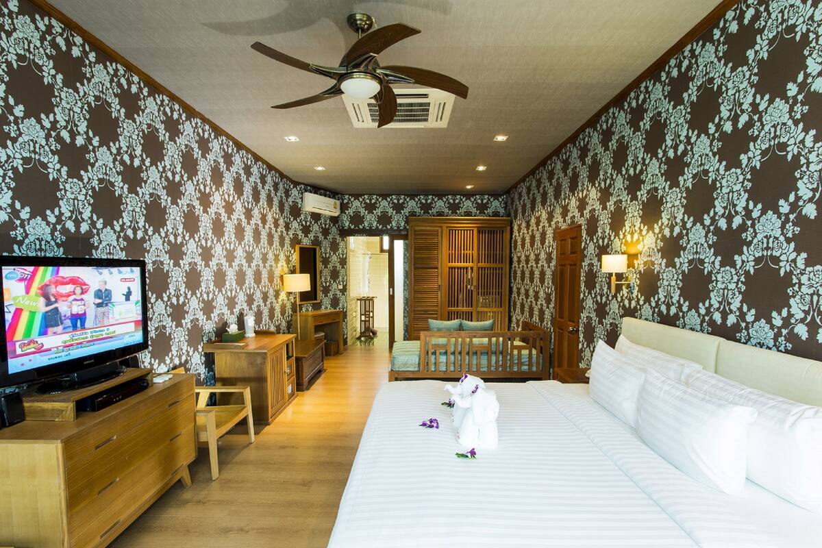 A hotel room with a large bed, wooden furniture, a television, and patterned wallpaper.
