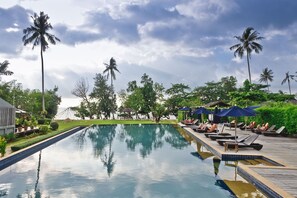 A poolside area with lounge chairs and umbrellas, surrounded by palm trees and a clear sky. - GajaPuri Resort Koh Chang (Ko Chang)