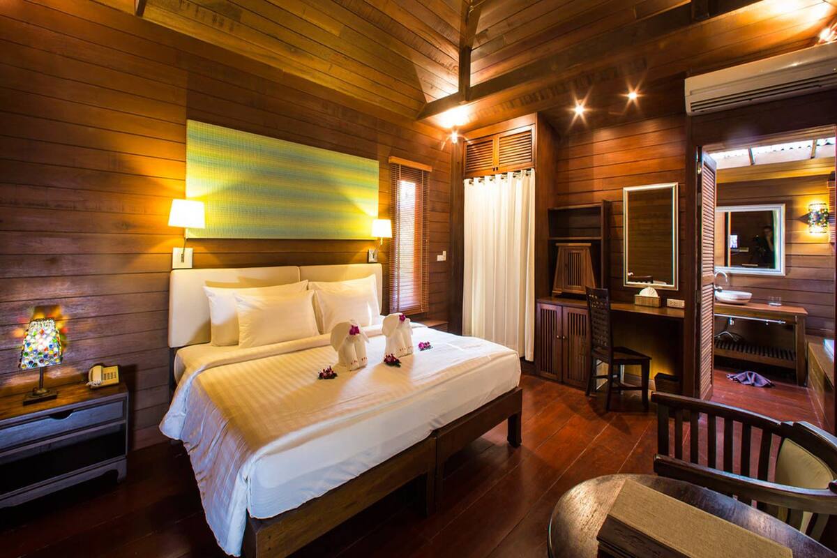 A wooden cabin-style bedroom with a large bed, bedside lamps, a mirror, and a wooden chair.