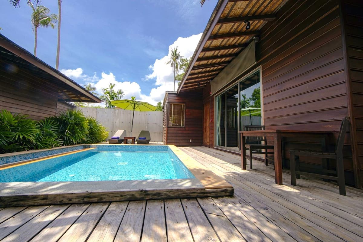 A wooden deck with a swimming pool, lounge chairs, and a covered seating area.
