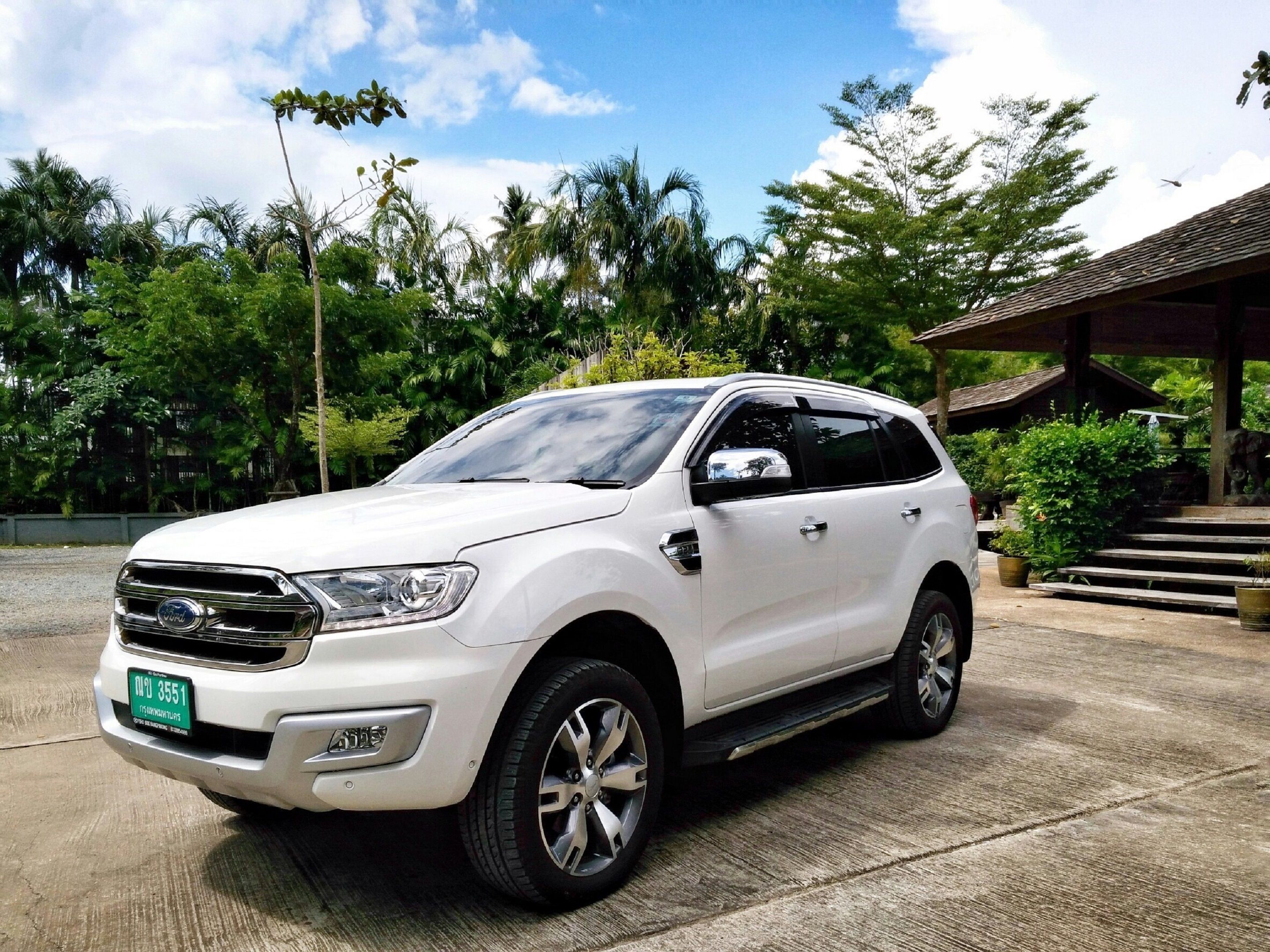 A white SUV parked in a covered area with steps leading up to a building, surrounded by lush greenery.