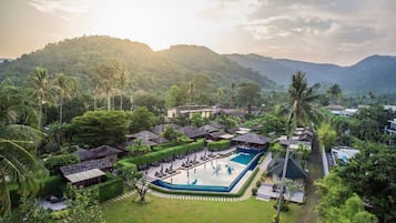 Relax in a tranquil setting surrounded by lush greenery and mountains, with a central swimming pool and thatched-roof bungalows.