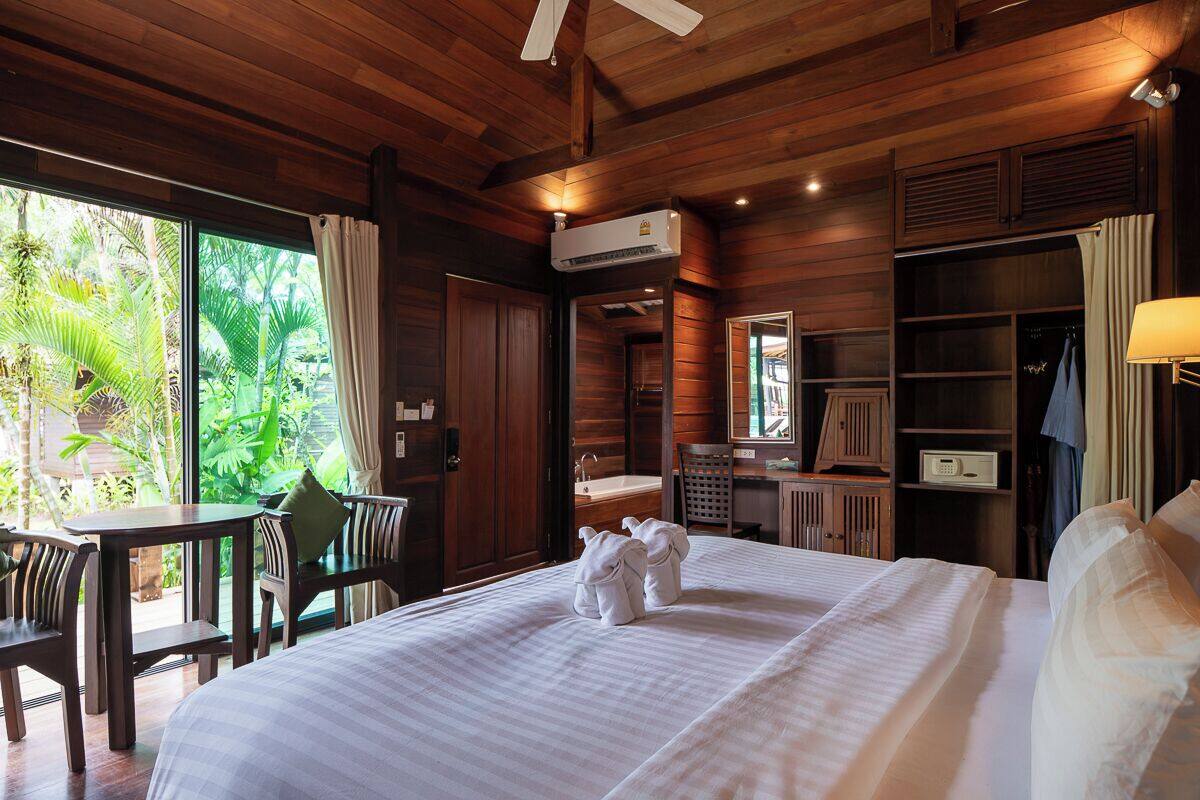 A wooden room with a bed, a desk, and a chair. There is a window with curtains, a ceiling fan, and an air conditioning unit.