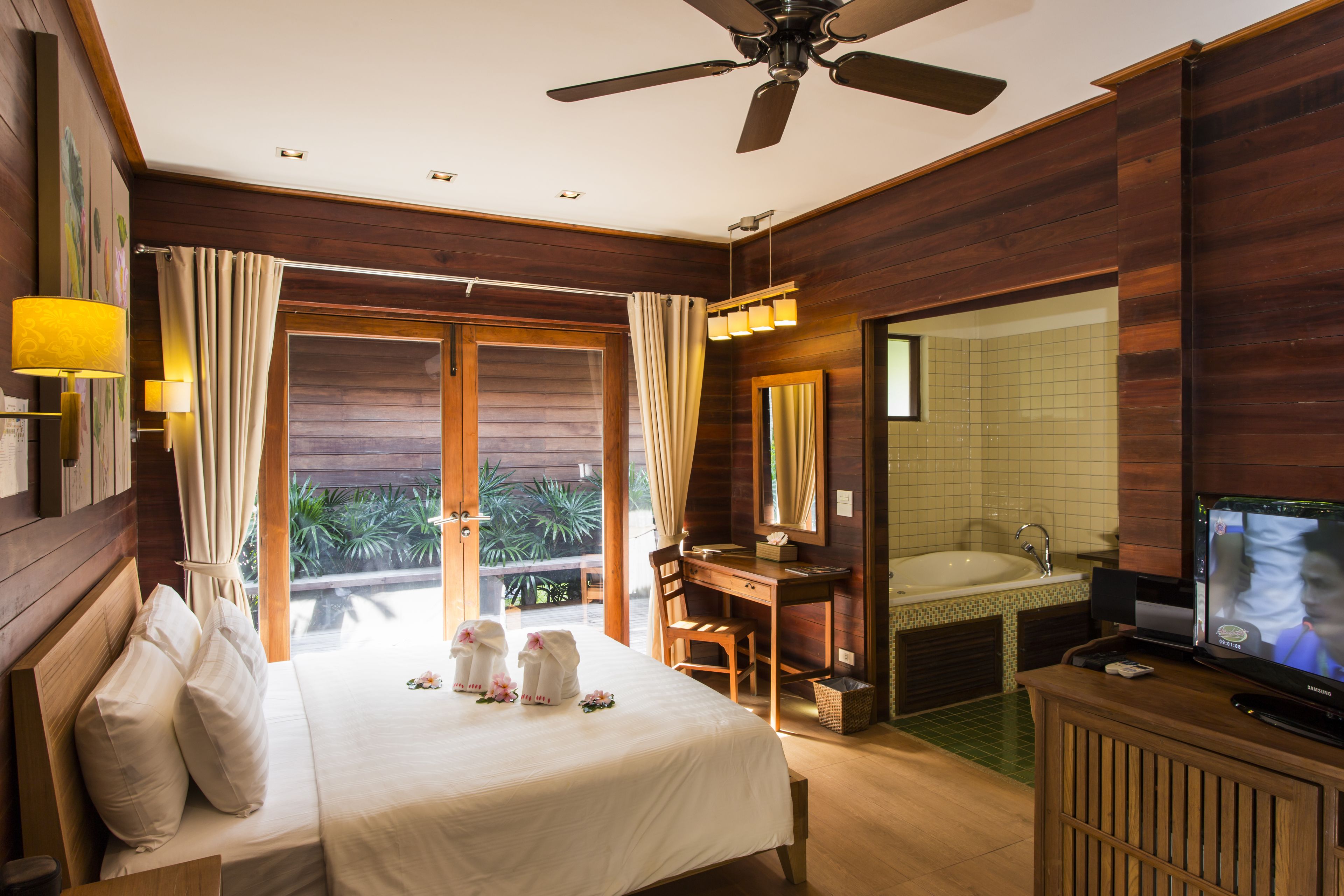 A hotel room with a bed, desk, chair, television, and a bathroom with a sink and mirror.