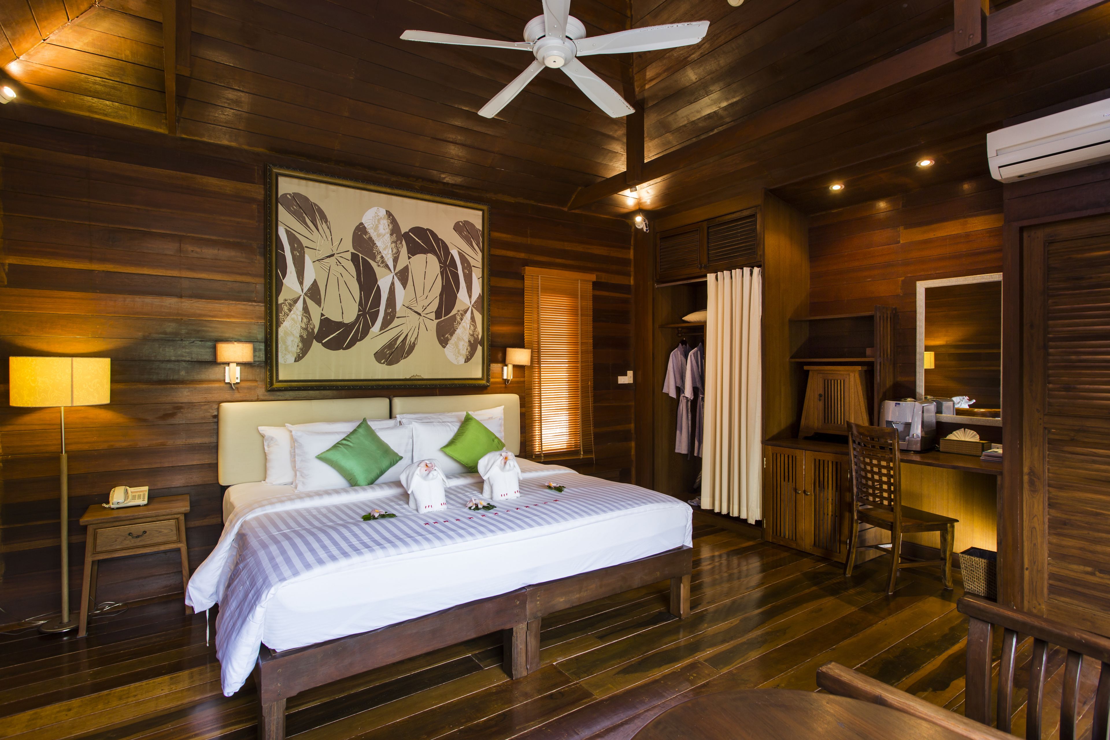 Habitación de hotel con piso de madera, una cama, ventilador de techo, escritorio y espejo.