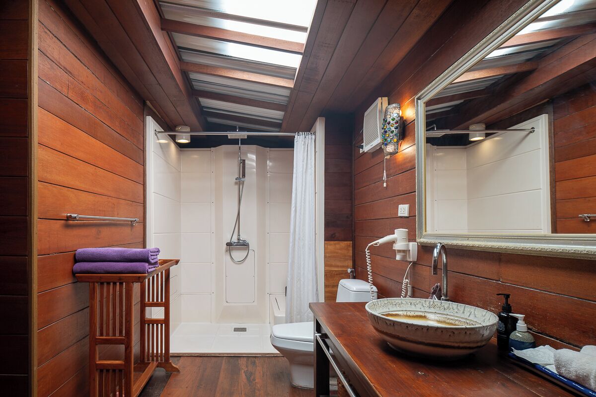 Une salle de bain aux murs lambrissés, équipée d’une douche, de toilettes et d’un lavabo.