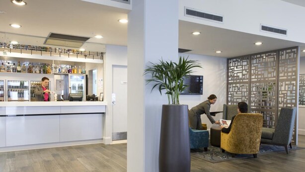 Un hall d’hôtel moderne comprenant un comptoir d’accueil, un espace salon et une plante décorative.