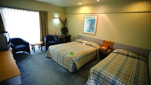 Une chambre d’hôtel avec deux lits, un bureau, une chaise, une petite table et une lampe.