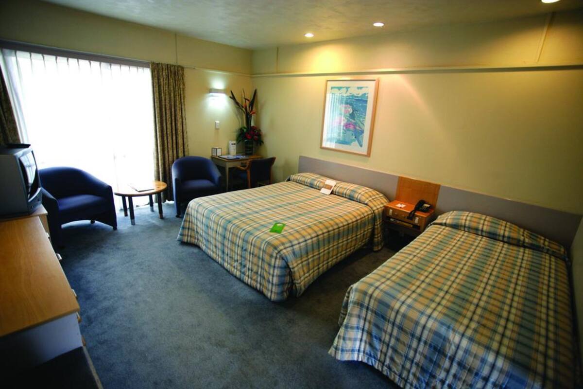 Ein Hotelzimmer mit zwei Betten, einem Schreibtisch, einem Stuhl, einem kleinen Tisch und einer Lampe.