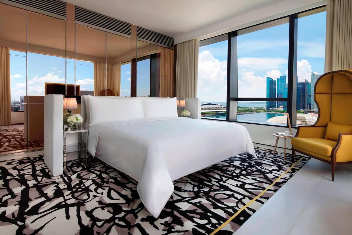 A modern hotel room with a large bed, a yellow armchair, and a city view.