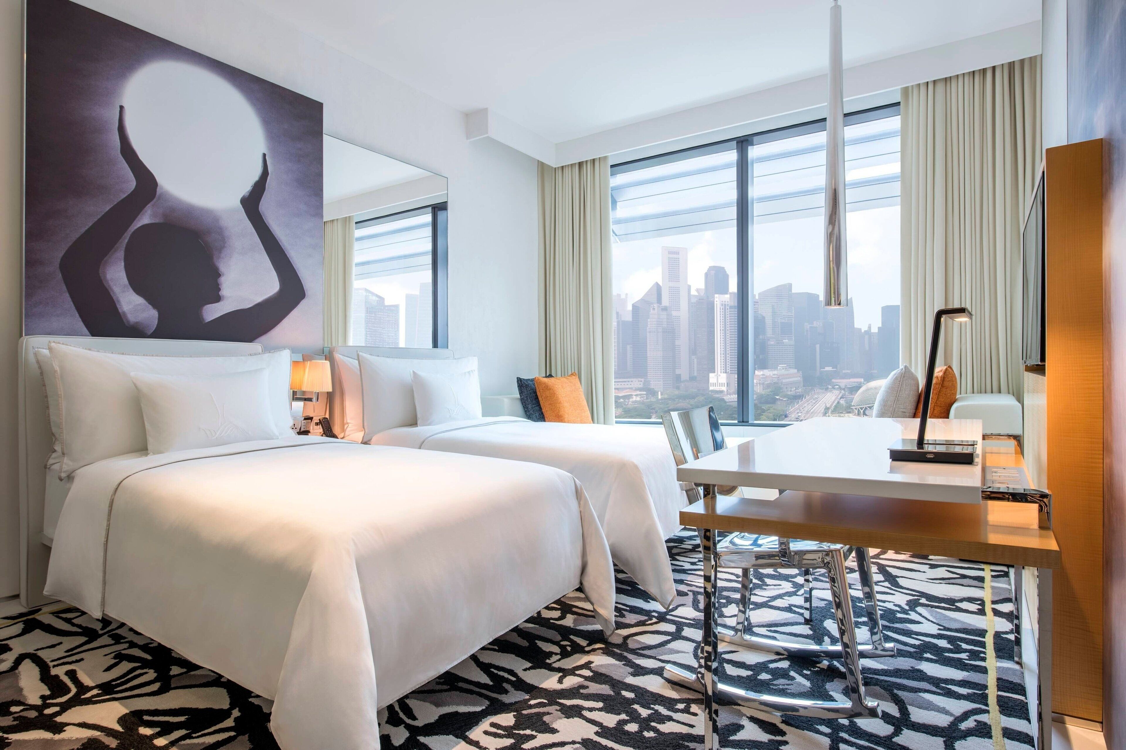 Een hotelkamer met twee bedden, een bureau en uitzicht op de stad.