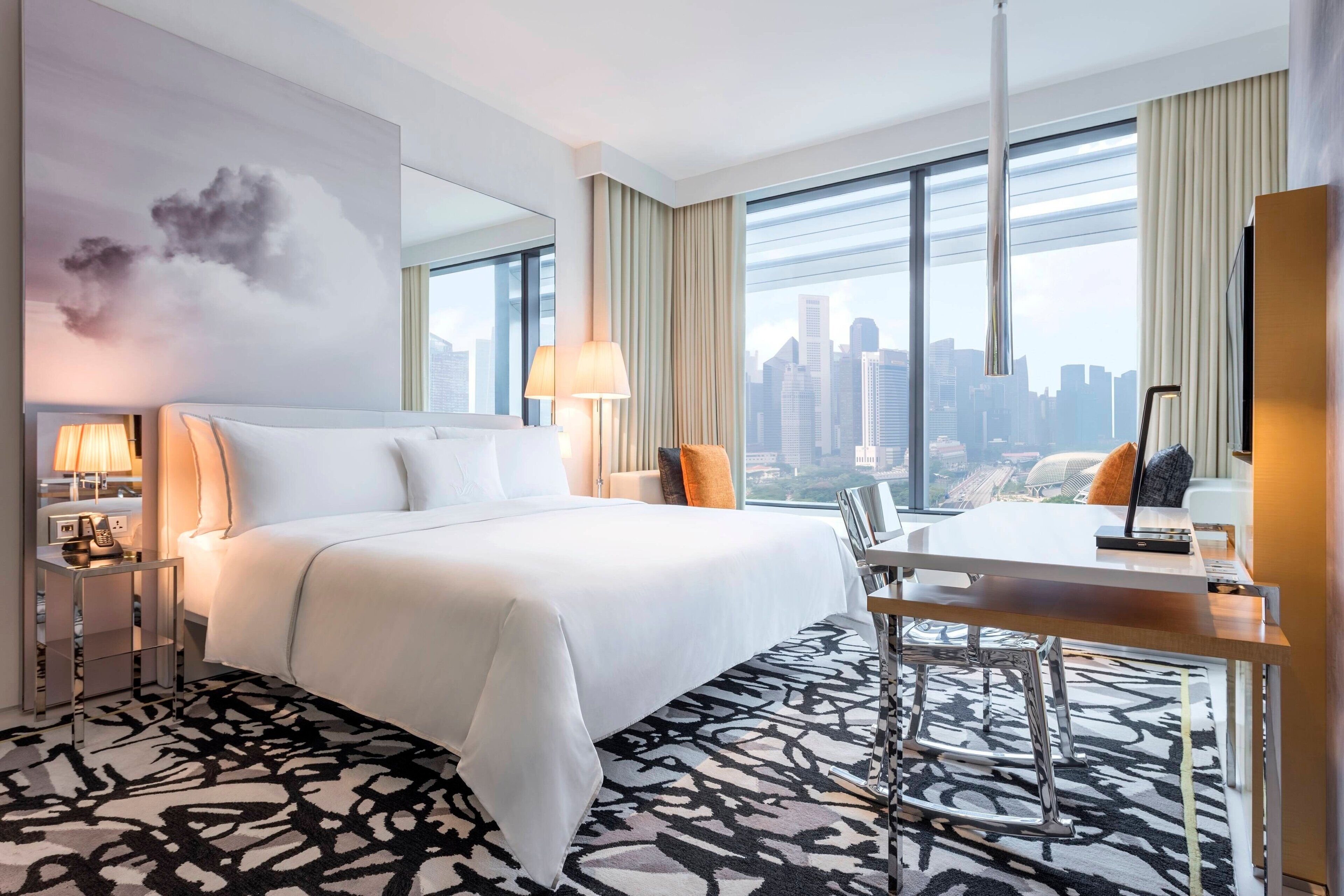 A hotel room with a large bed, a desk, and a view of the city skyline.