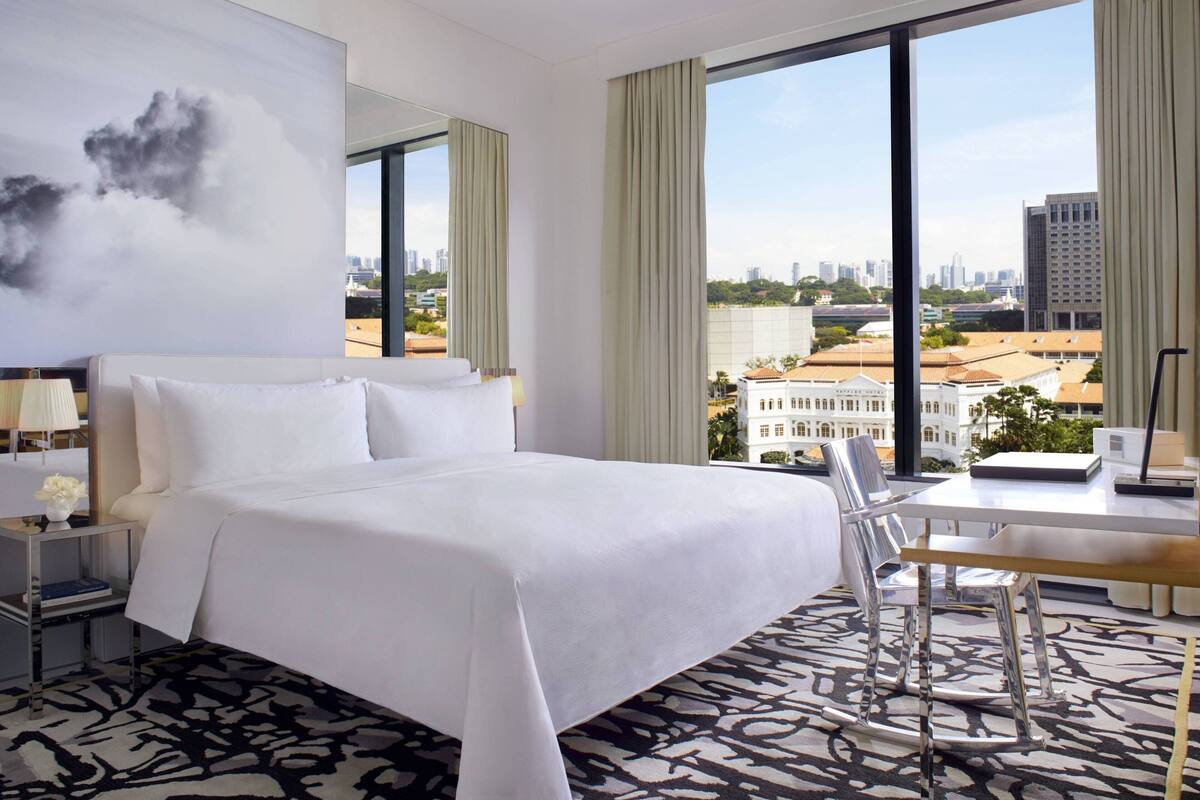 A hotel room with a large bed, a desk, and a chair. The room has a view of a cityscape and a river.