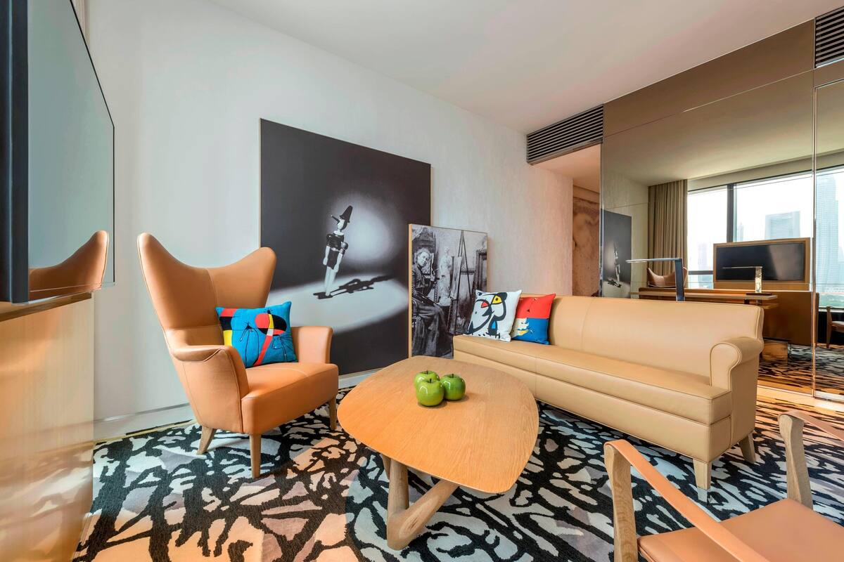 A modern hotel room with a sofa, armchair, and a coffee table.
