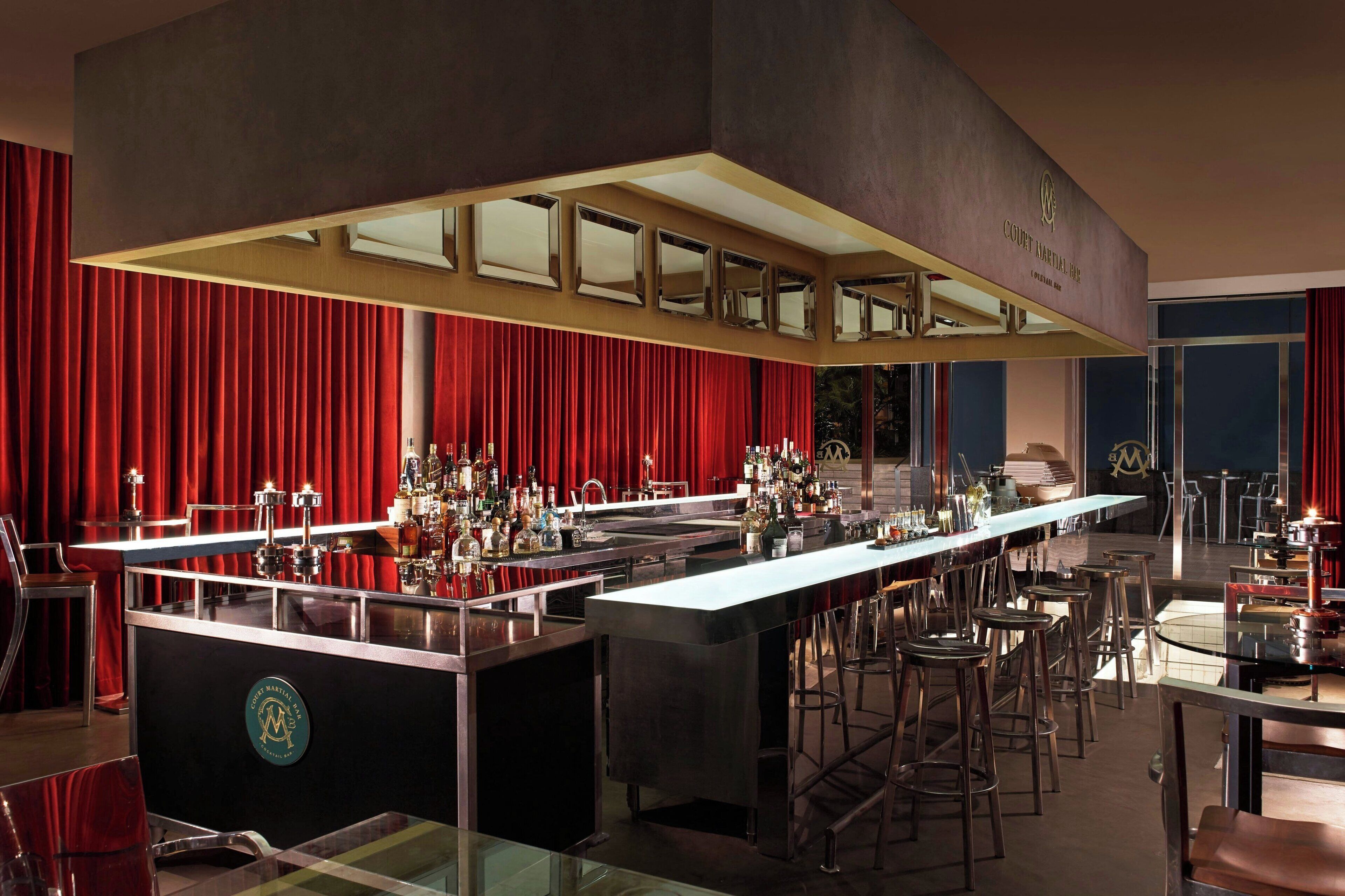 A bar area with a long counter, multiple stools, and a backdrop of red curtains.