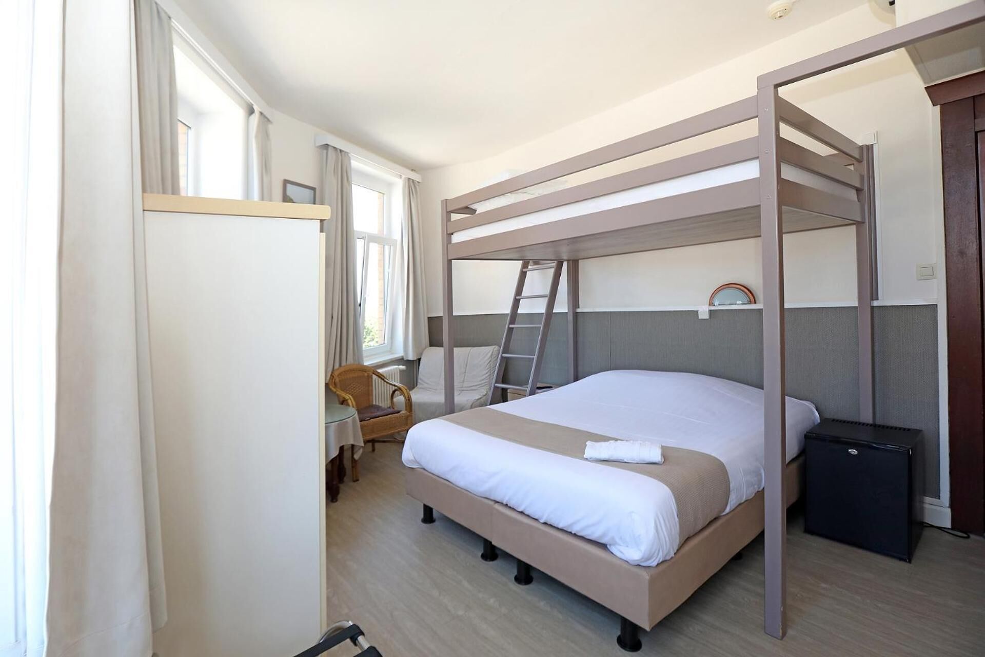 Ein Einzelzimmer mit Stockbett, Schreibtisch, Stuhl, einem kleinen Tisch, einer Stehleiter und einem Mülleimer.