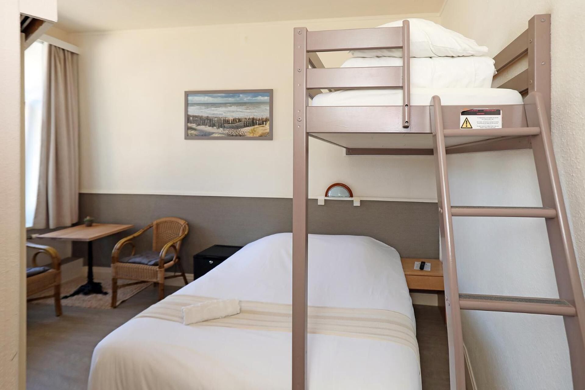 Una camera con letto a castello, una scrivania e una sedia, un quadro appeso al muro e una finestra con tende.