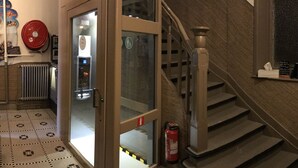 A staircase with a fire extinguisher, a glass door with a fire alarm, and patterned floor tiles. - Hotel Cecil (De Panne)