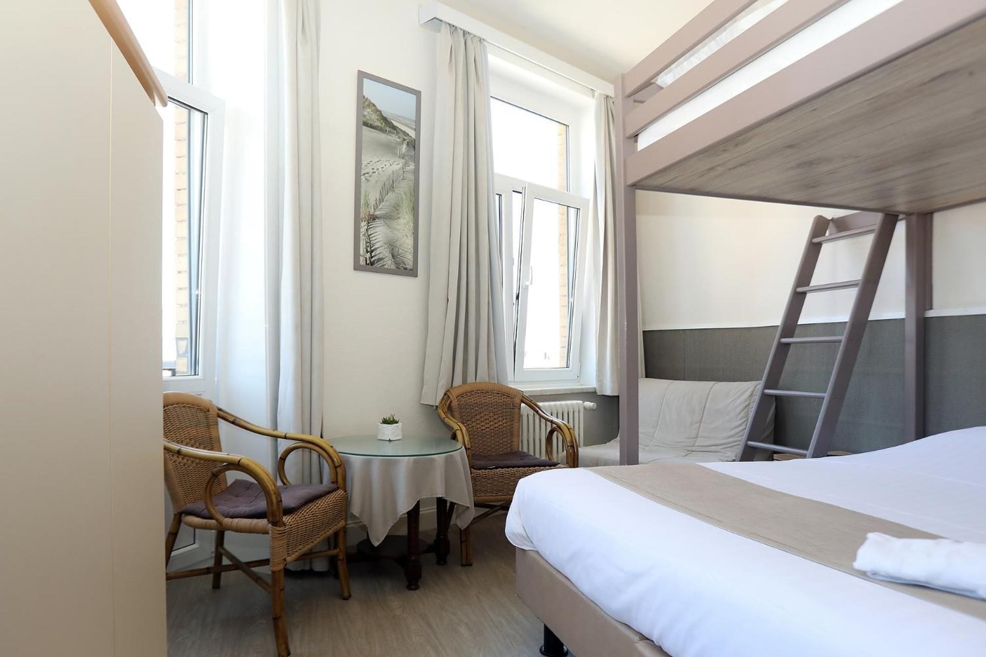 A hotel room with a bunk bed, a small table with chairs, and a window with curtains.