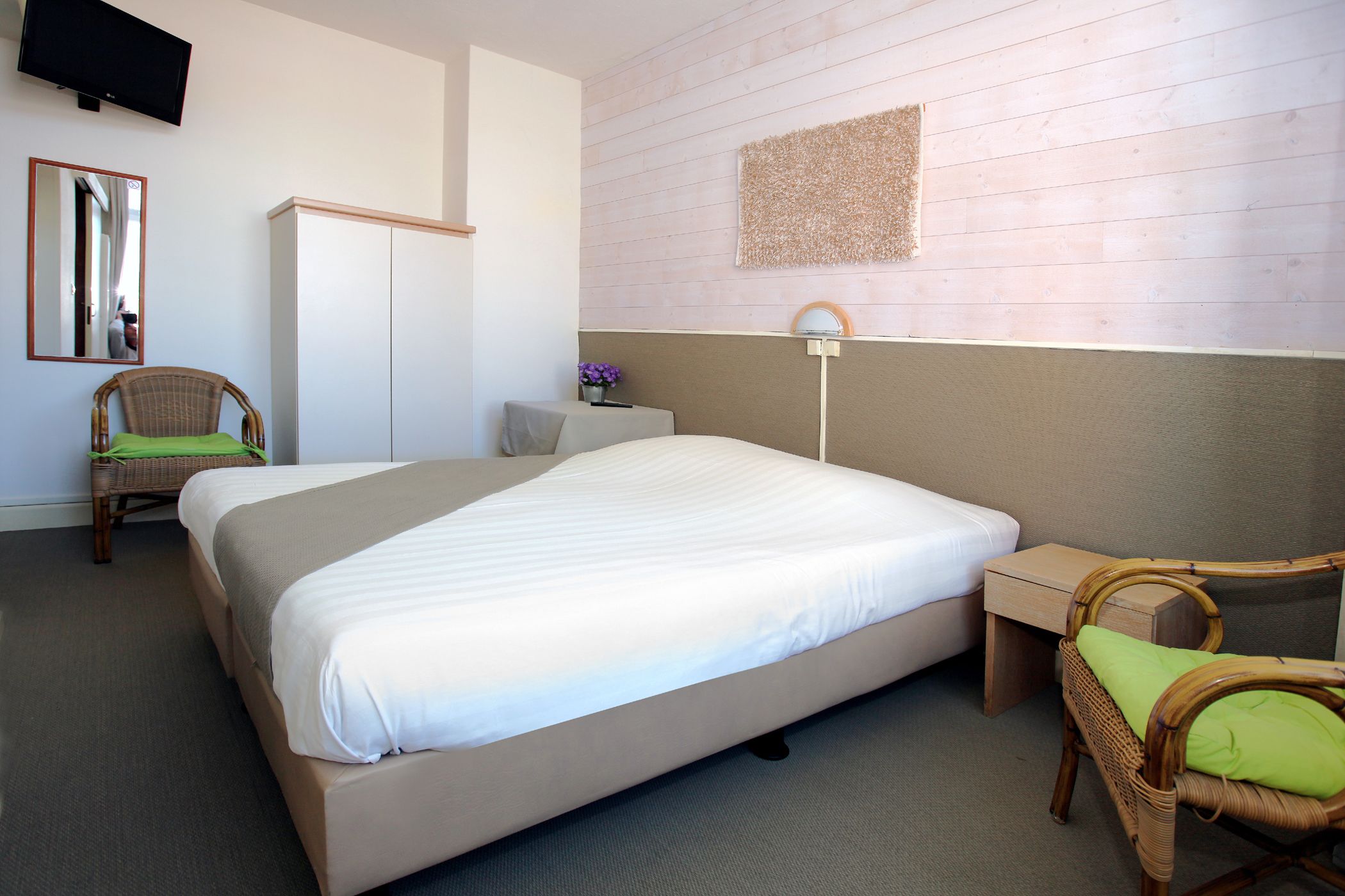 Une chambre d’hôtel avec un grand lit, un bureau, une chaise, une télévision et un miroir.