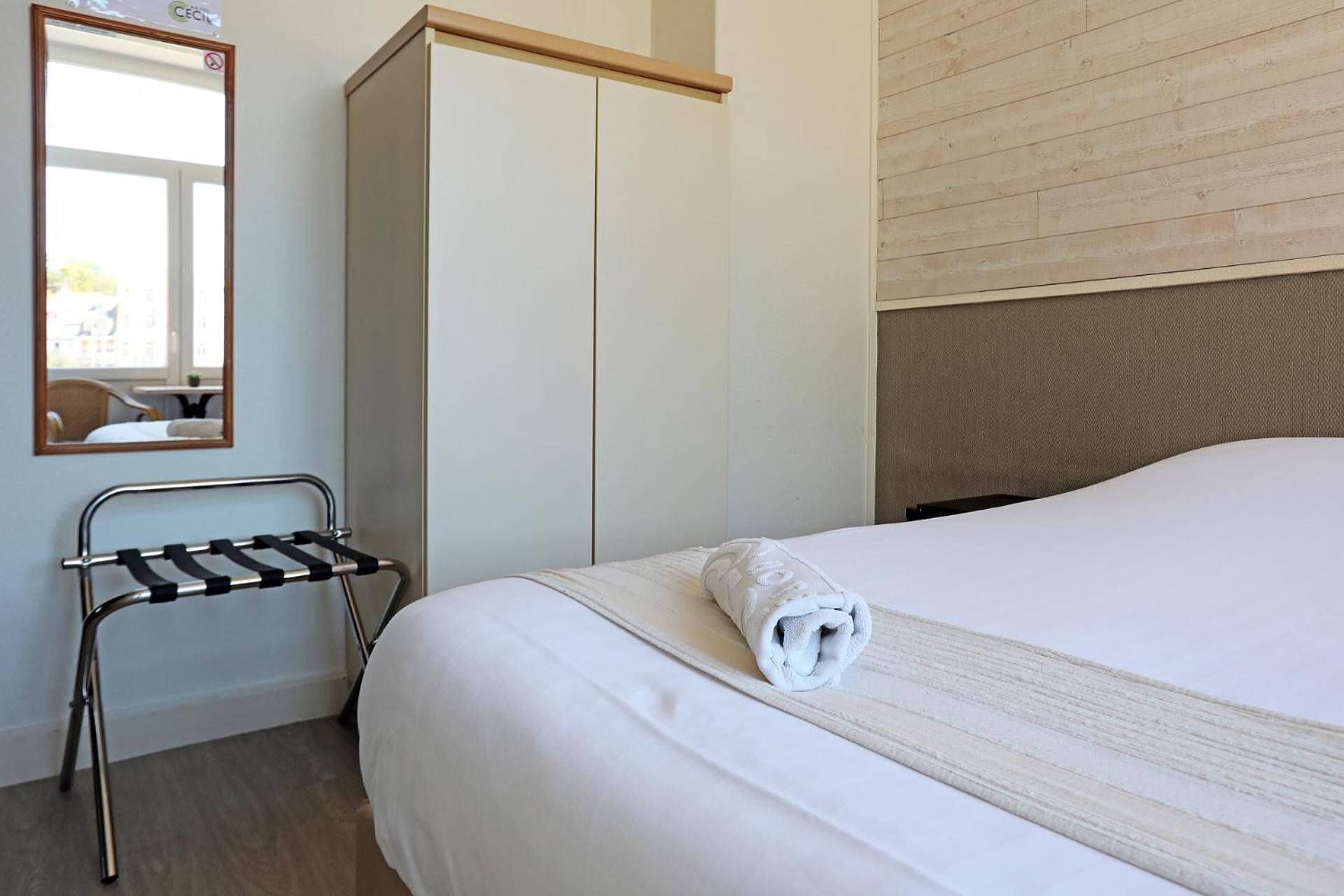 Una habitación de hotel con una cama, cabecera de madera, armario, espejo y toallero.