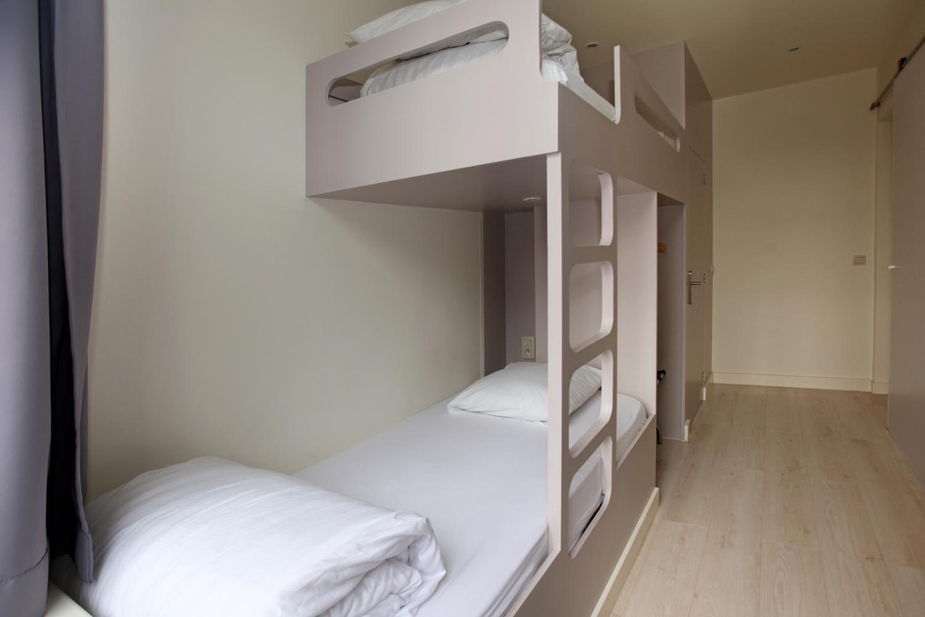 A bunk bed room with a wooden floor, a door, and a white wall.