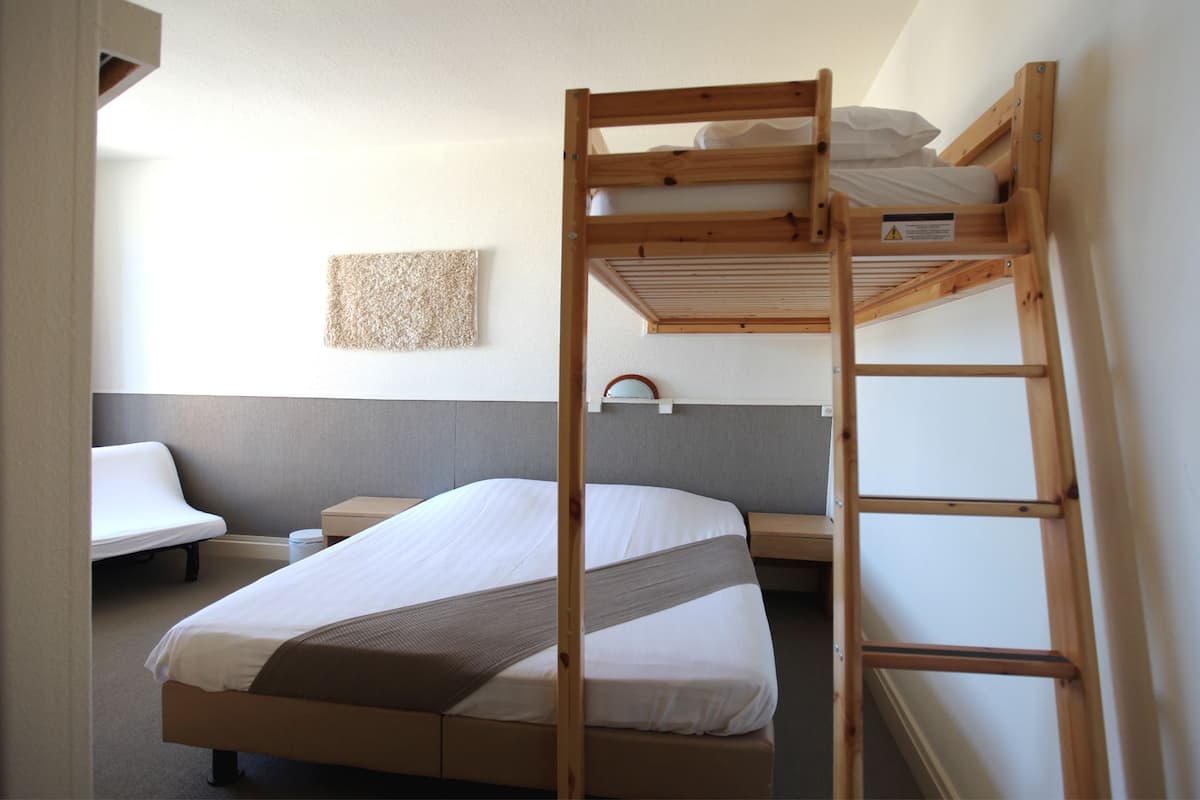 Une chambre avec un lit superposé, une échelle, une table de chevet et une étagère fixée au mur.