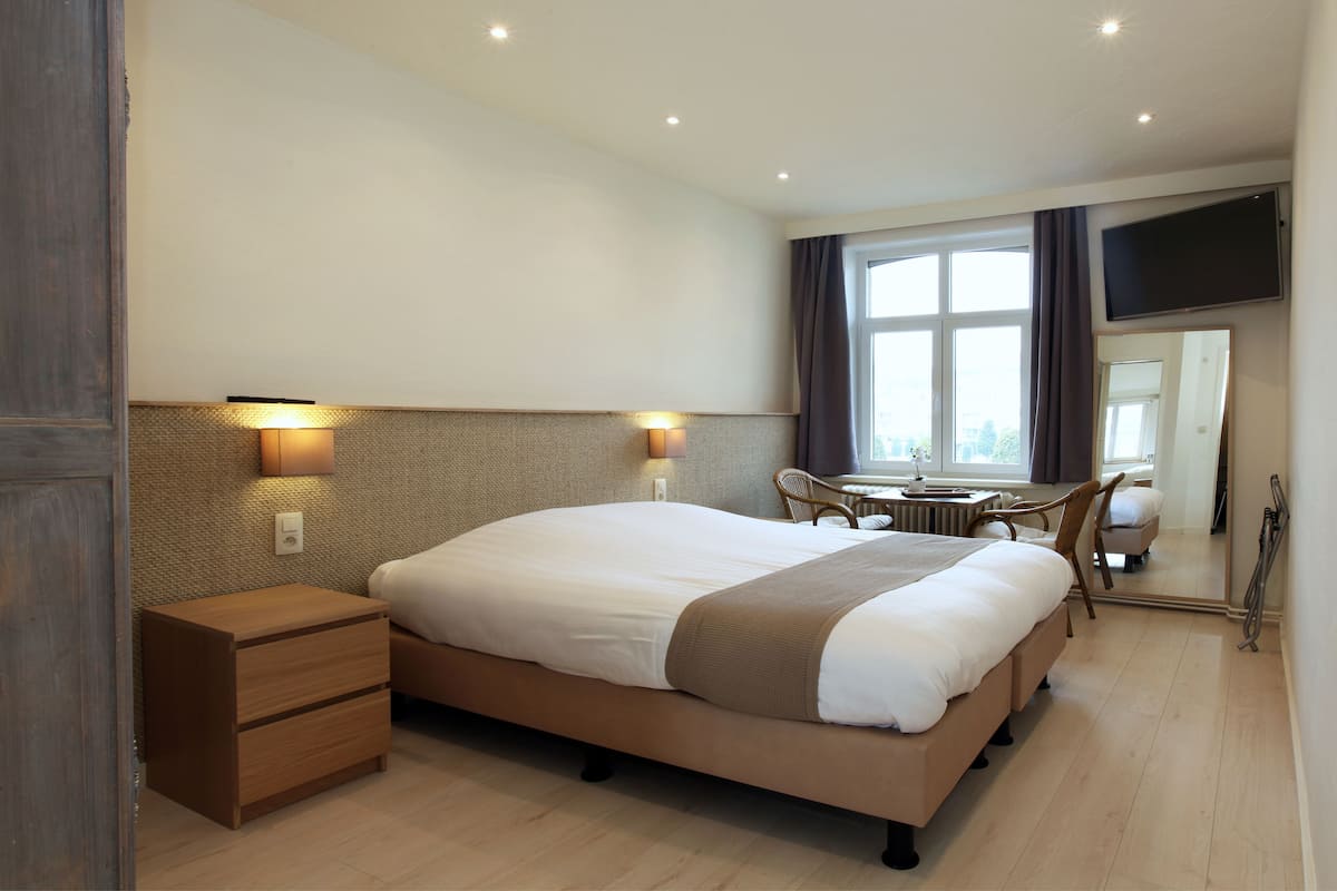 Une chambre d’hôtel dotée d’un grand lit, de tables de chevet, d’un bureau avec une chaise, d’un téléviseur à écran plat et d’une grande fenêtre avec des rideaux.