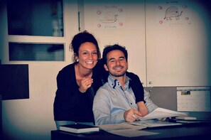 Two people sitting at a desk with papers, in a room with a whiteboard and a calendar. - Hotel Cecil (De Panne)