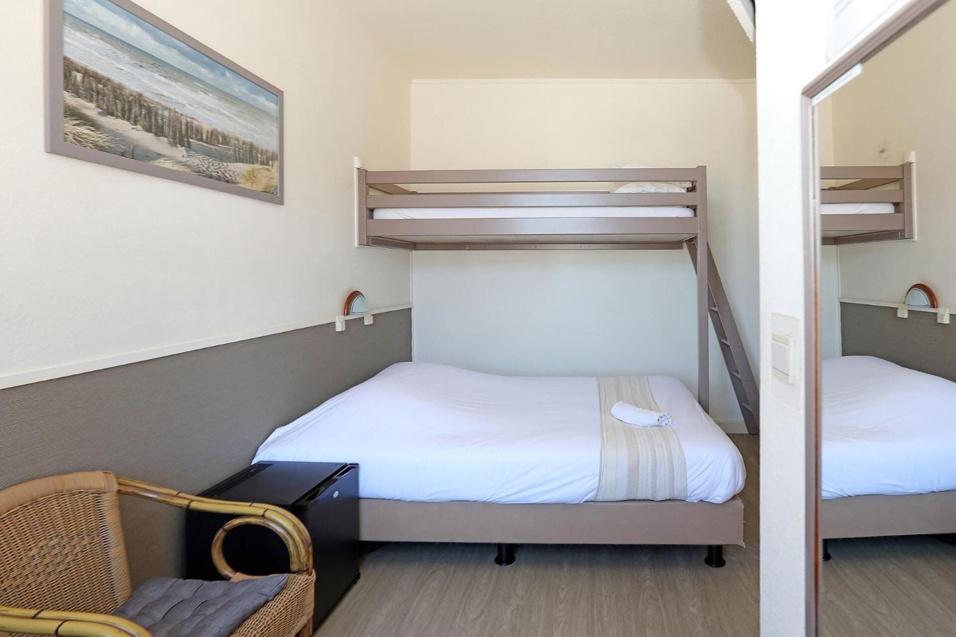 Una habitación con literas, una cama individual, una mesita pequeña, una silla y un cuadro en la pared.