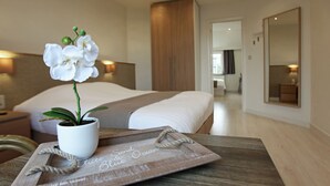 A hotel room with a bed, a wooden side table with a tray, a potted orchid, and a mirror. - Hotel Cecil (De Panne)