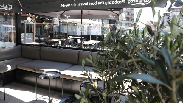 An outdoor seating area with a sofa and tables, overlooking a street. - Hotel Cecil (De Panne)