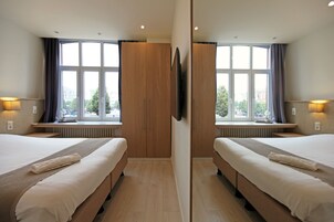 Habitación de hotel con espejos, dos camas, un ventanal con cortinas, un televisor de pantalla plana y un radiador debajo de la ventana.