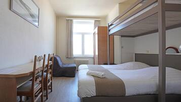 Una habitación de hotel con literas, un escritorio con sillas, una ventana con cortinas y un radiador.