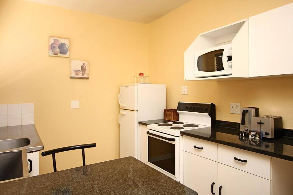 A compact kitchen with white cabinets, a stove, a microwave, and a toaster.