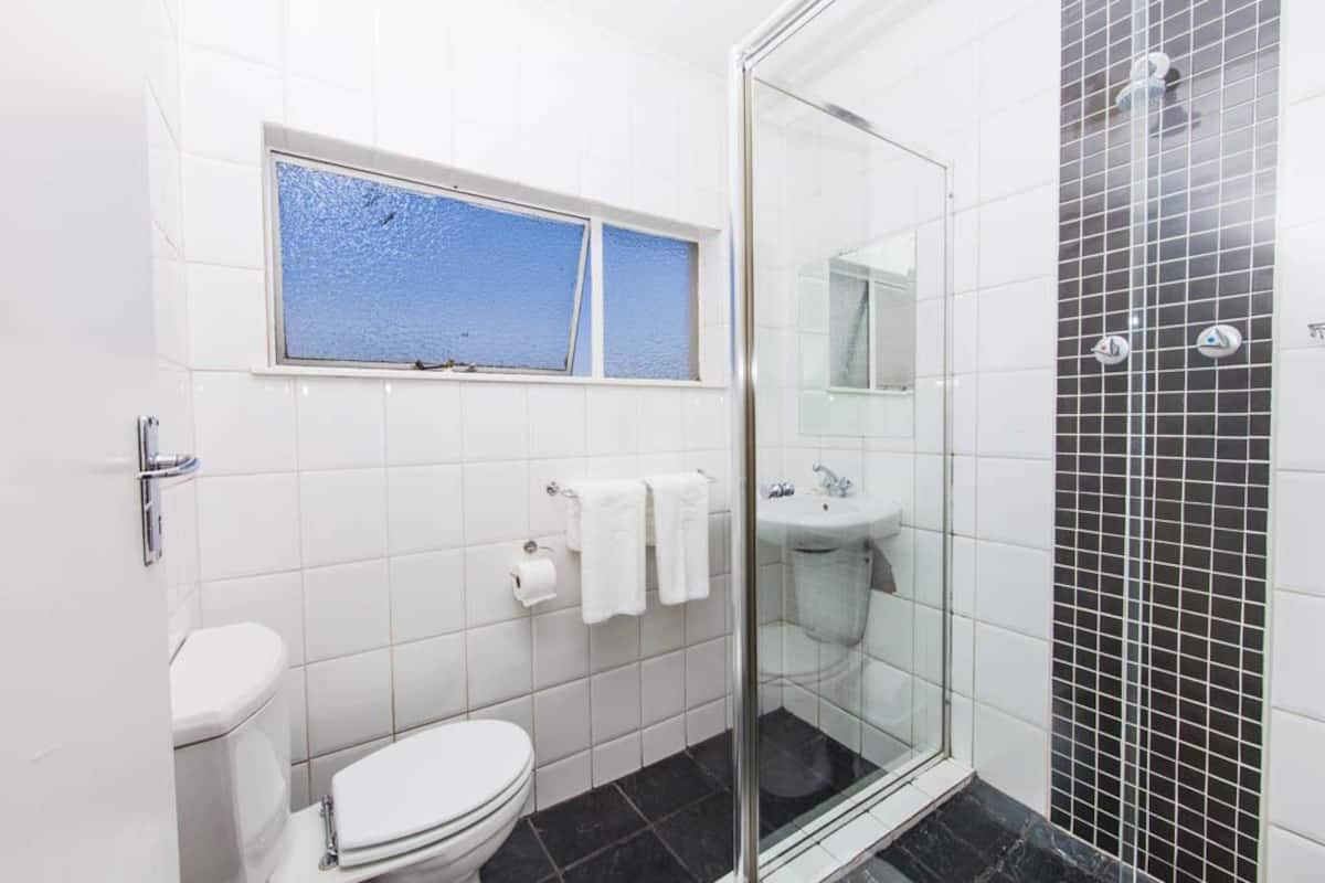 A bathroom with a toilet, a sink, a shower with a glass door, and a window above the toilet.