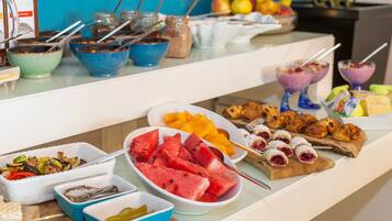 Ein Buffet mit verschiedenen Speisen, darunter Obst, Gebäck und ein Salat.
