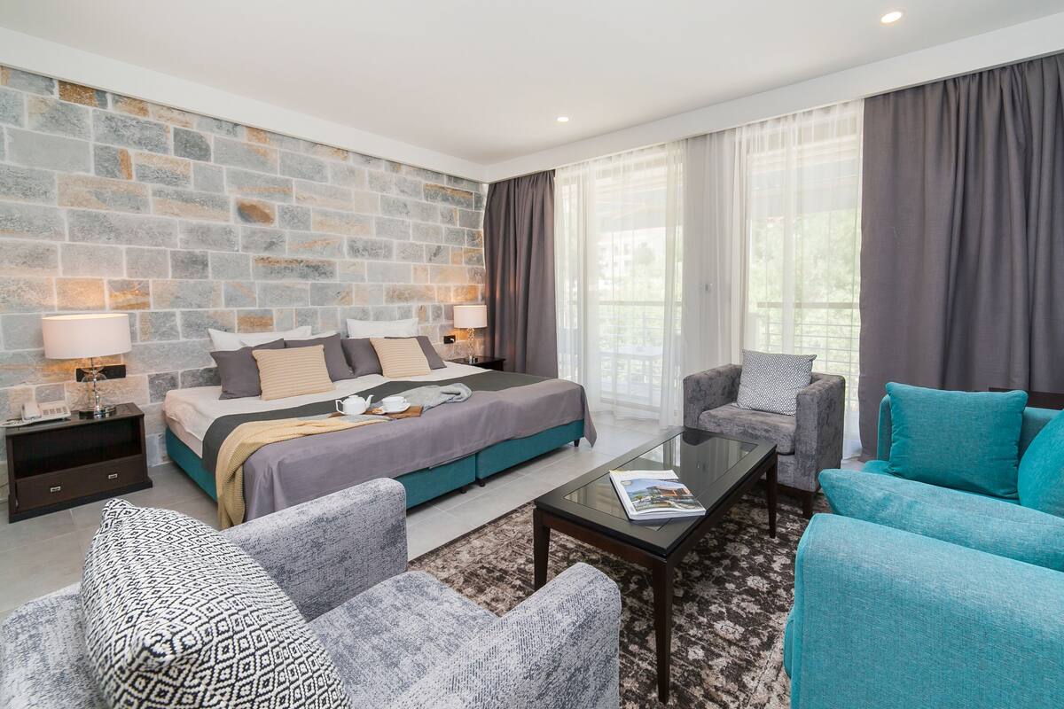 Een moderne hotelkamer met een stenen accentmuur, een groot bed, grijs en blauw gestoffeerde meubels en een glazen bijzettafeltje.
