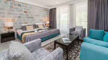 Une chambre d’hôtel moderne avec un mur d’accent en pierre, un grand lit, des meubles rembourrés aux tons de gris et de bleu, et une table basse en verre.