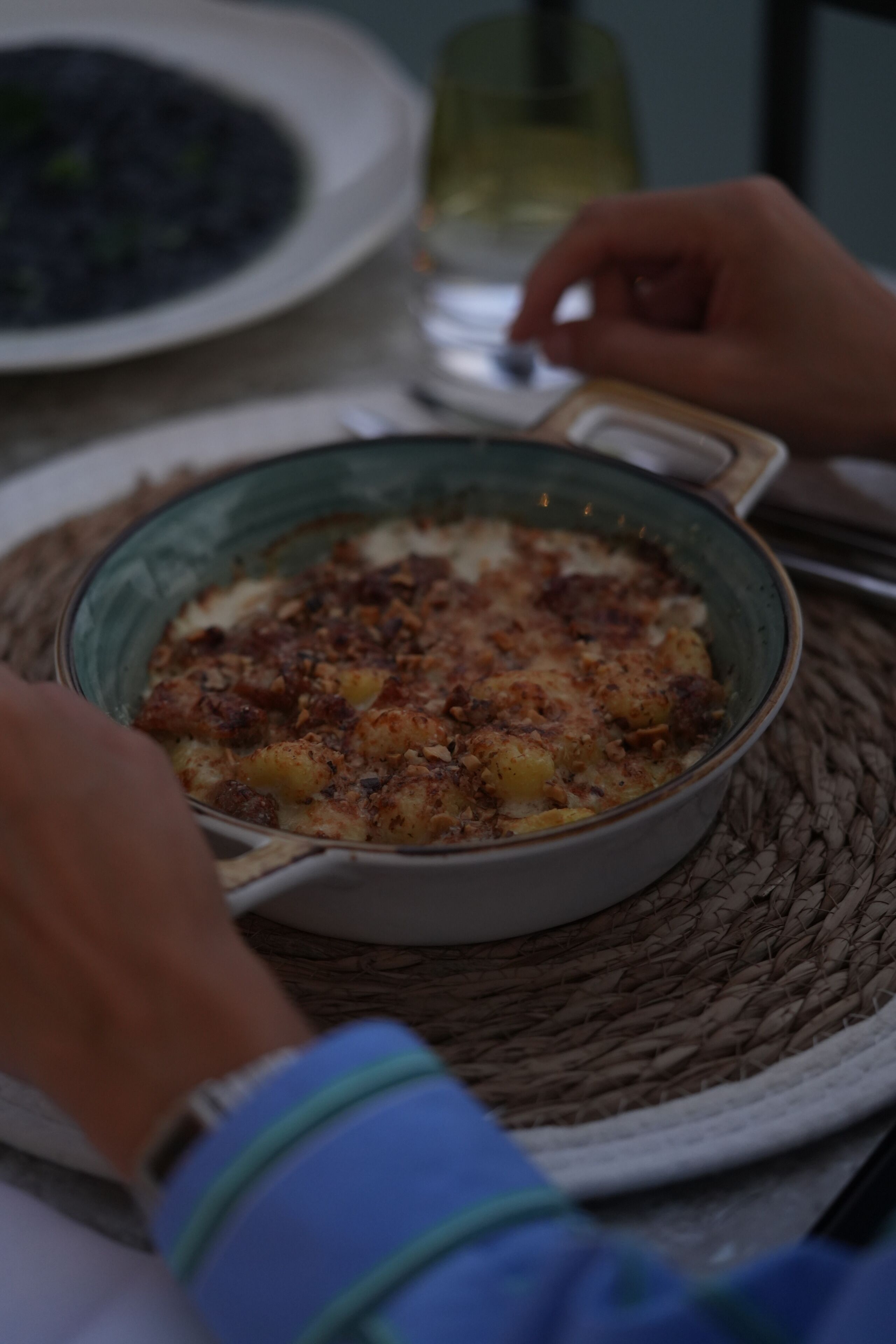 Une personne tient dans ses mains une assiette contenant un plat cuit au four, peut-être un gratin, posée sur un set de table en fibres tressées.