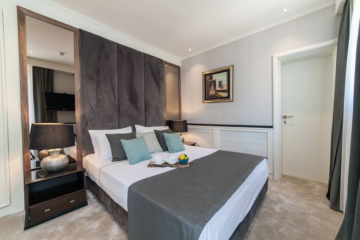 Een moderne slaapkamer met een groot bed, nachtkastjes, een flatscreen televisie en een ingelijst kunstwerk aan de muur.