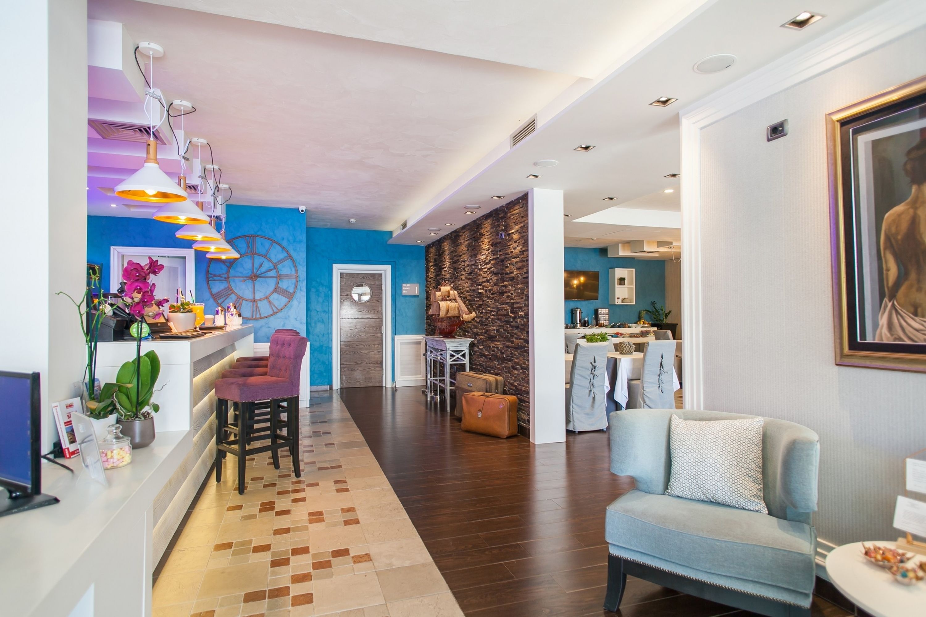 A modern hotel lobby with a reception desk, seating area, and a dining space.