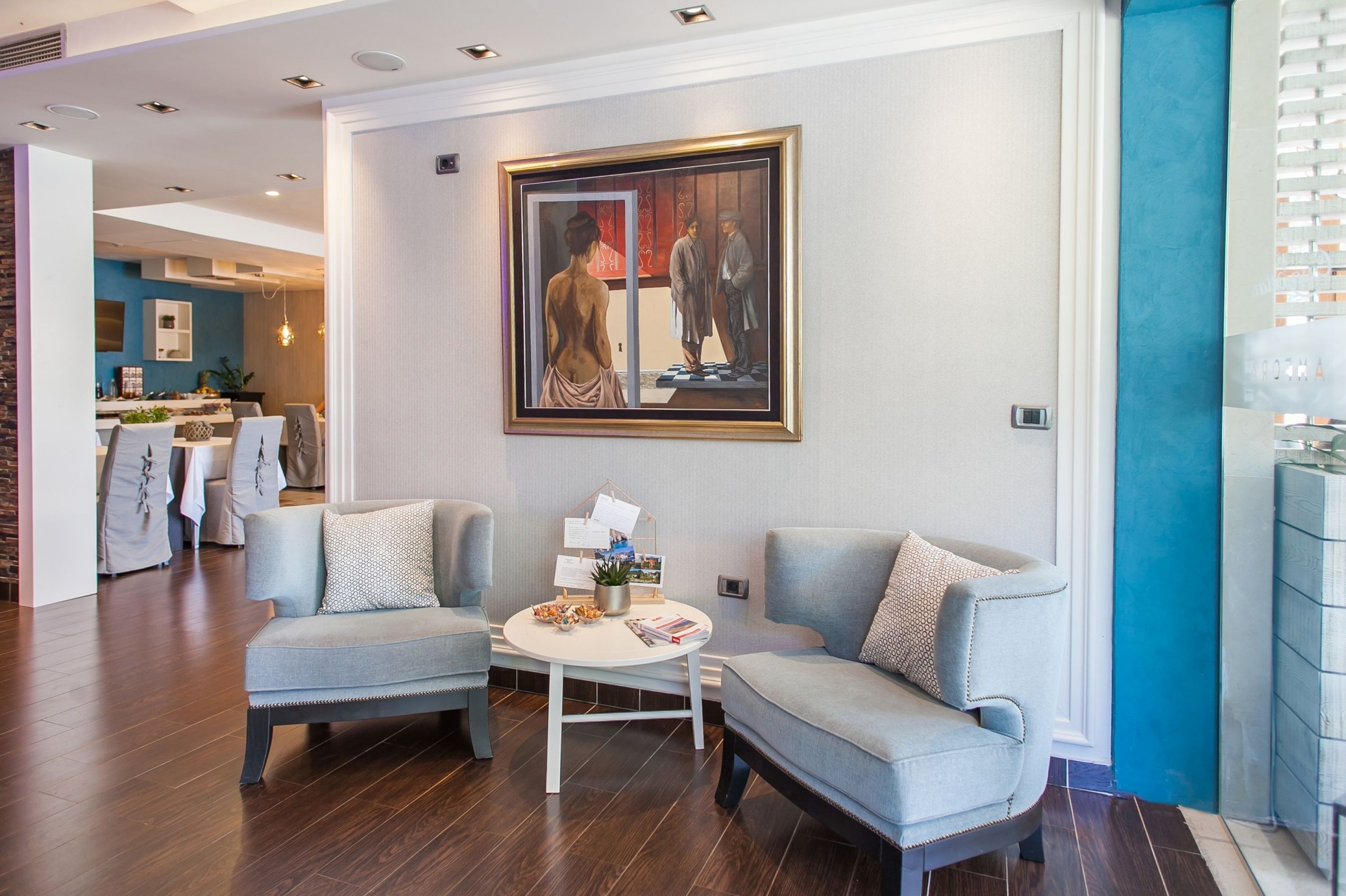 Un moderno vestíbulo de hotel con dos sillones grises, una mesa redonda con una planta pequeña y un cuadro en la pared.