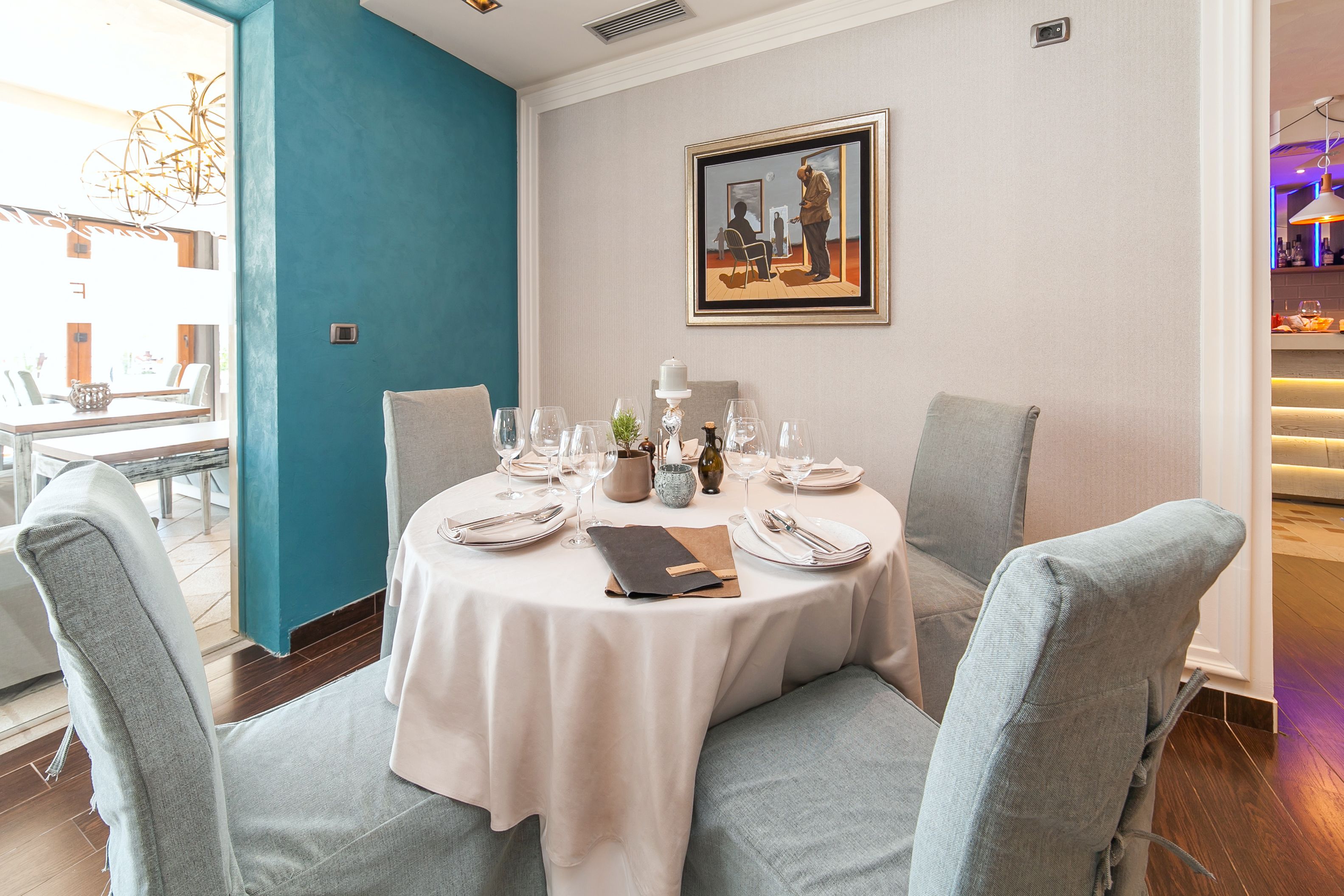 A dining area with a round table set for four, chairs, and a painting on the wall.