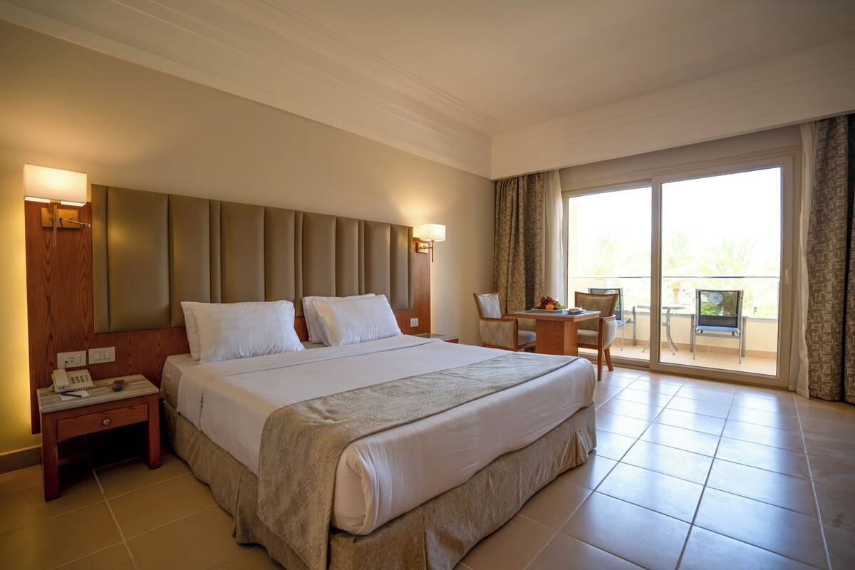 Une chambre d’hôtel avec un grand lit, un bureau avec une chaise, un téléphone et une vue sur l’extérieur grâce à une porte-fenêtre coulissante.